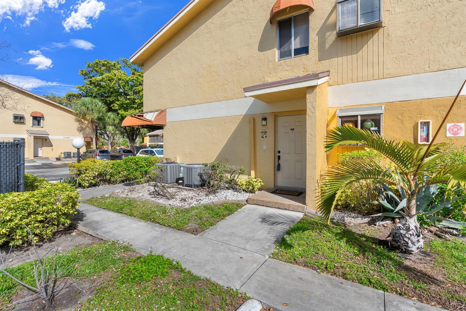 A yellow two-story apartment building features a front entrance, concrete walkway, and landscaping — 3053 N Oakland Forest Drive # 102, Oakland Park FL 33309, OAKLAND PARK, FL