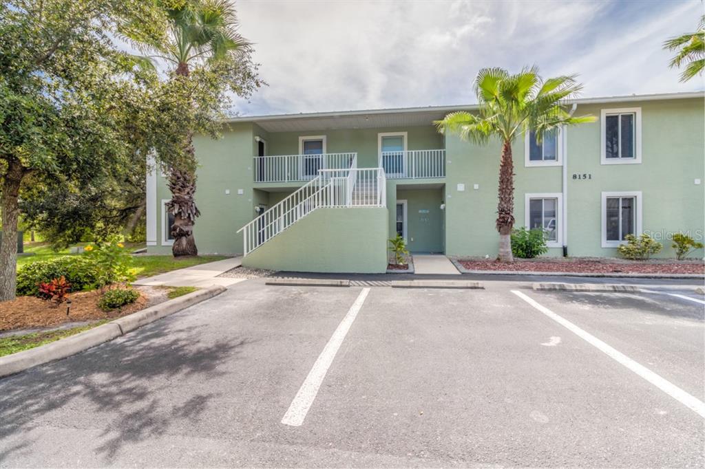 A two-story green apartment building features an exterior staircase, balconies, and a paved parking lot — 8151 MEMORY LANE UNIT 118, ROTONDA WEST, FL
