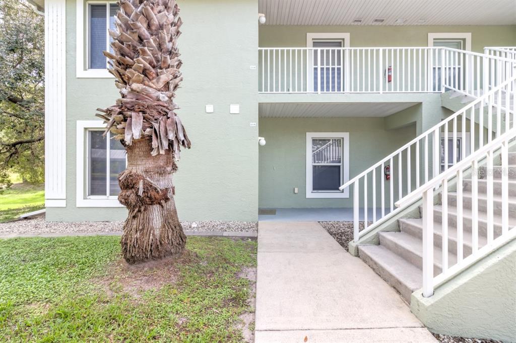 An exterior view of a two-story apartment building with a palm tree and stairs — 8151 MEMORY LANE UNIT 118, ROTONDA WEST, FL