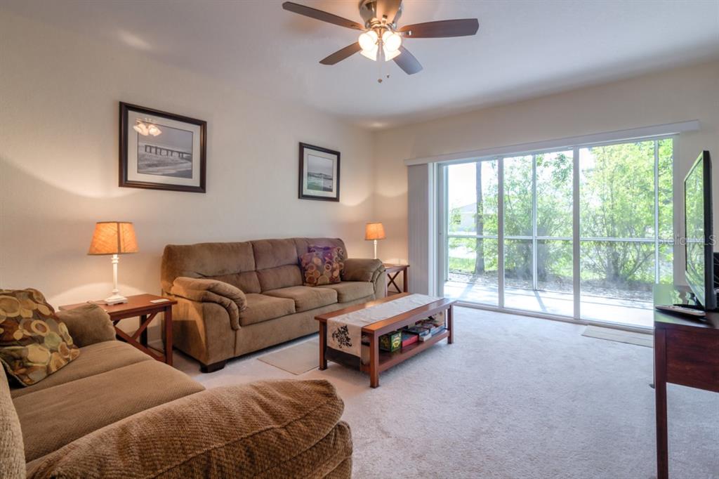 A living room with brown sofas, a coffee table, and sliding glass doors to a patio — 8151 MEMORY LANE UNIT 118, ROTONDA WEST, FL
