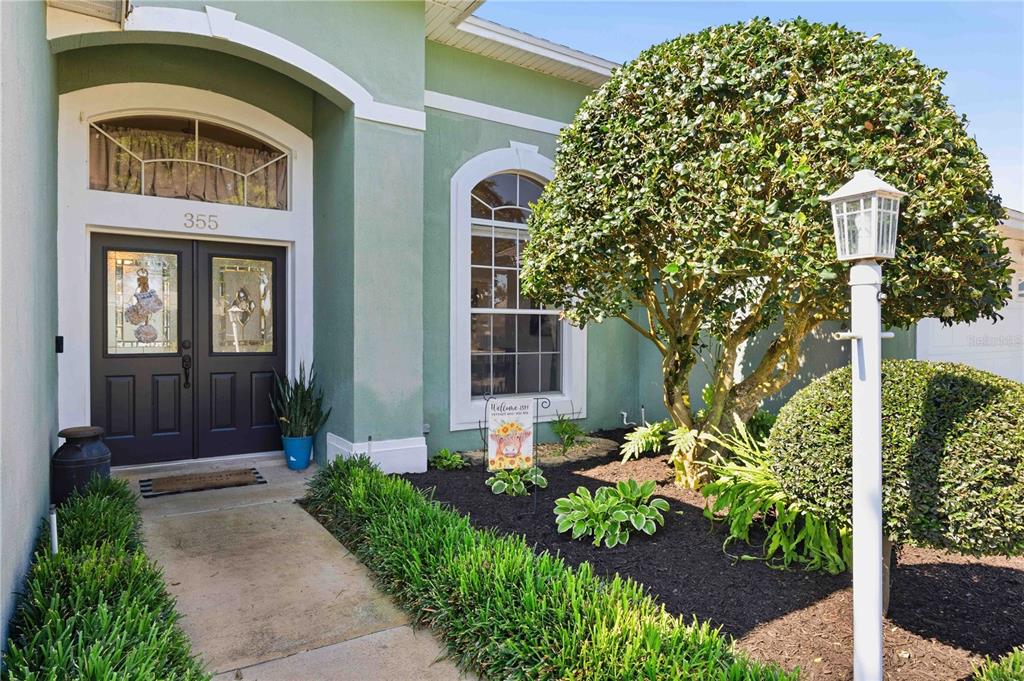 A green house exterior features a double front door, a large window, and landscaping — 355 RUBY LAKE LOOP, WINTER HAVEN, FL