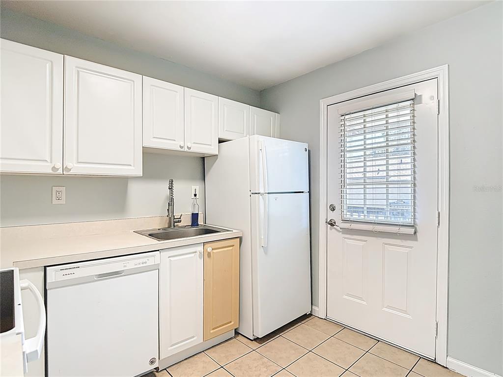 A kitchen features white cabinets, a dishwasher, a refrigerator, a sink, and a glass-paneled door — 201 PINE VIOLET COURT UNIT 201, TAMPA, FL