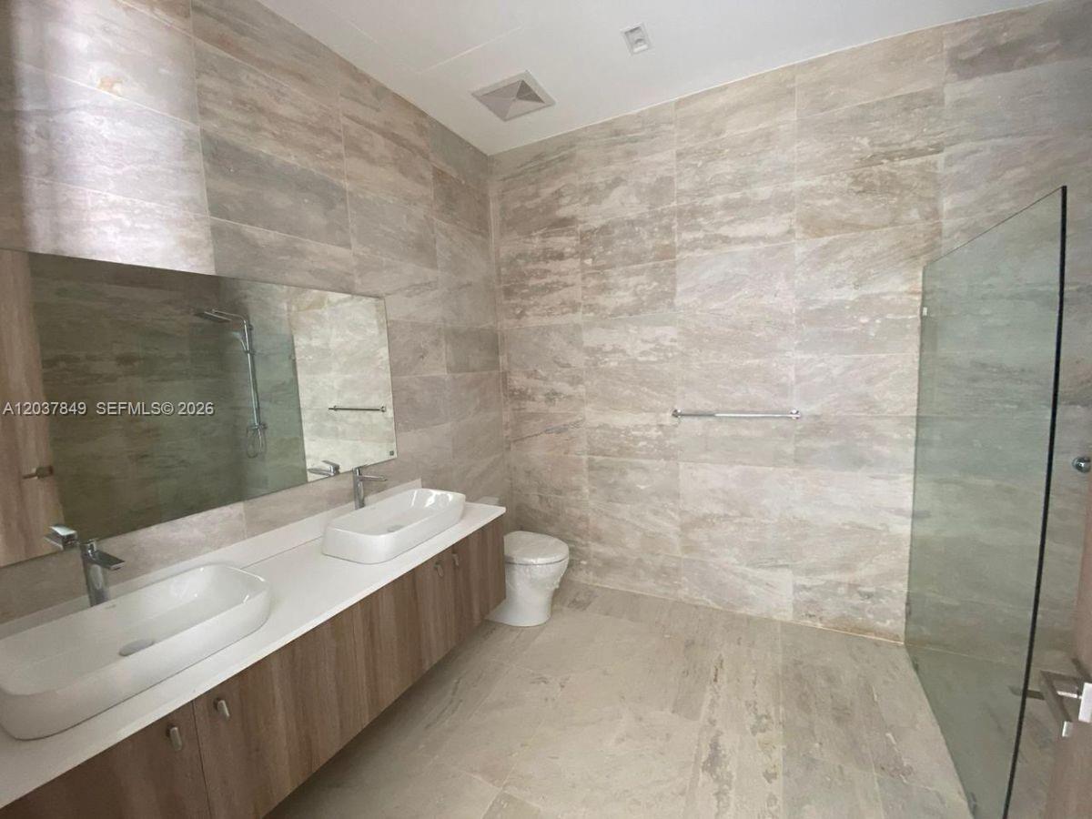 A modern bathroom features a double vanity, a glass-enclosed shower, and light-colored stone tiling — 0 las palmitas, FL