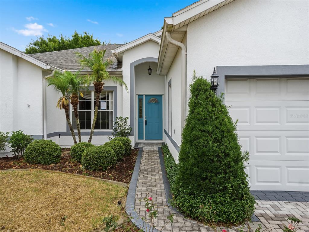 A white house exterior features a blue front door, a brick walkway, and landscaping — 4835 SABLE RIDGE COURT, LEESBURG, FL