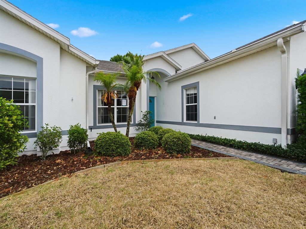 A single-story house exterior features white stucco walls, gray trim, and a paved walkway — 4835 SABLE RIDGE COURT, LEESBURG, FL