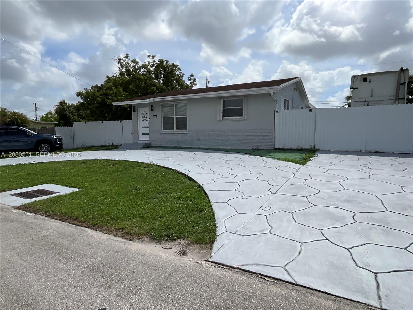 A single-story house features a light gray exterior, a white door, and a patterned driveway — 1905 SW 100th Ave, Miramar FL 33025, MIRAMAR, FL