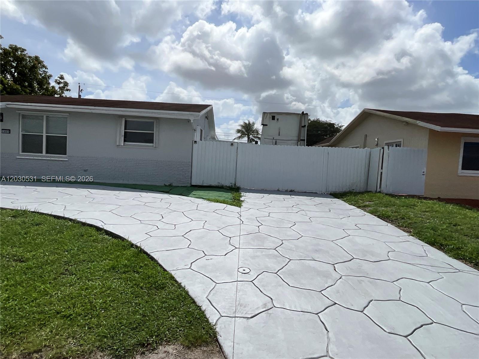 A gray house with a patterned concrete driveway and a white fence between two homes — 1905 SW 100th Ave, Miramar FL 33025, MIRAMAR, FL