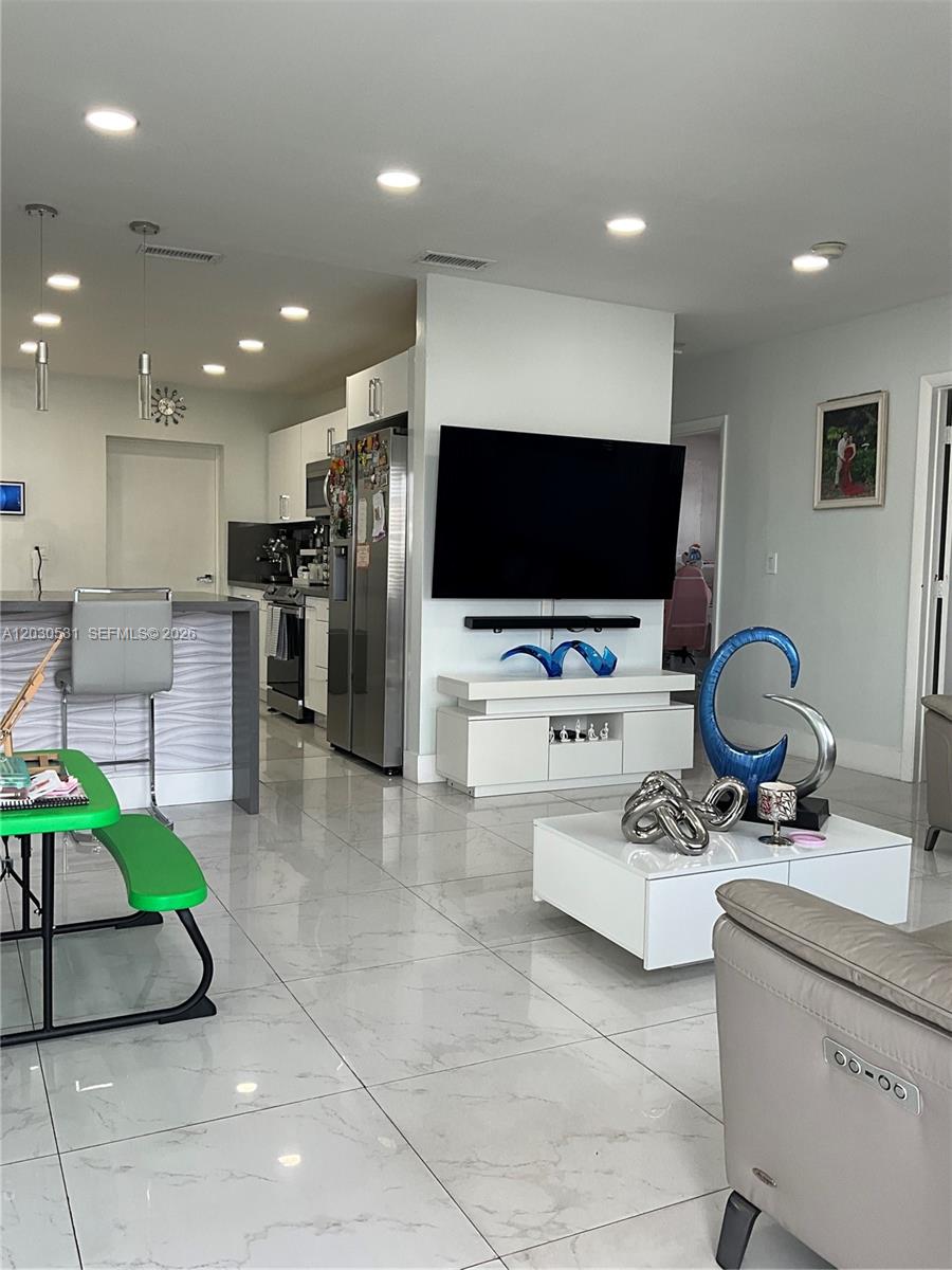 A modern open-concept living room features white tile floors, a wall-mounted television, and a kitchen — 1905 SW 100th Ave, Miramar FL 33025, MIRAMAR, FL