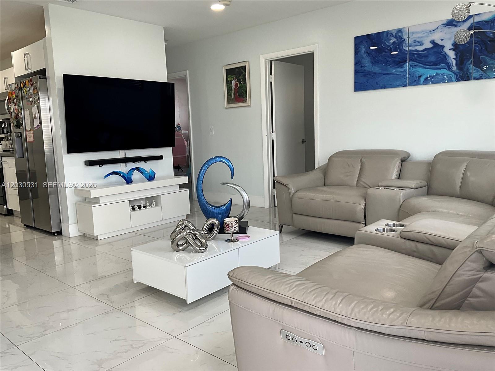 A living room features a wall-mounted television, white furniture, and light-colored leather sectional seating — 1905 SW 100th Ave, Miramar FL 33025, MIRAMAR, FL