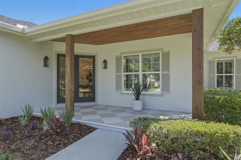 A covered front porch features a checkered floor, wood-paneled ceiling, and double glass entry doors — 9589 PINE LILY STREET, ORLANDO, FL