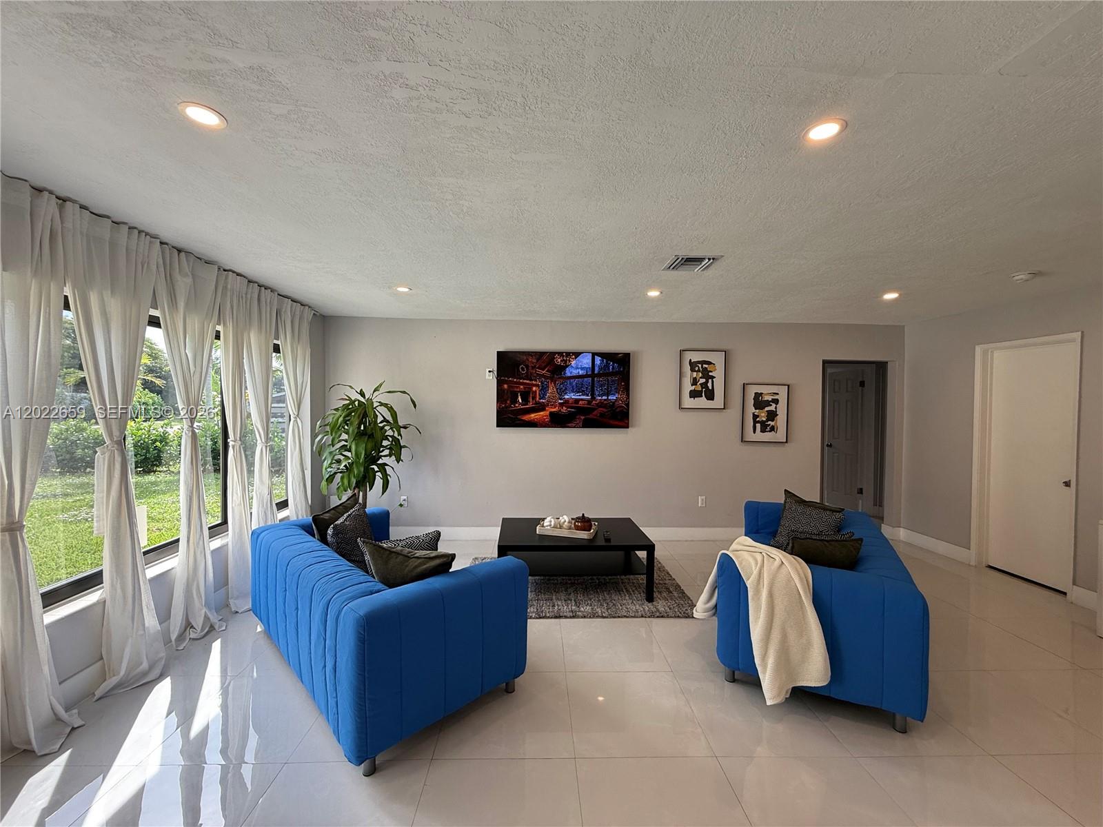 A living room features two blue sofas, a black coffee table, and large floor-to-ceiling windows — 1825 SW 43rd Ave, Fort Lauderdale FL 33317, FORT LAUDERDALE, FL