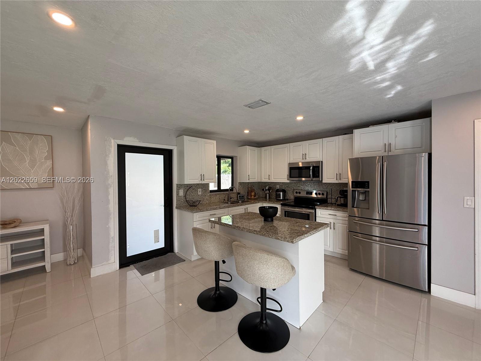 A kitchen features white cabinetry, granite countertops, stainless steel appliances, and a central island — 1825 SW 43rd Ave, Fort Lauderdale FL 33317, FORT LAUDERDALE, FL