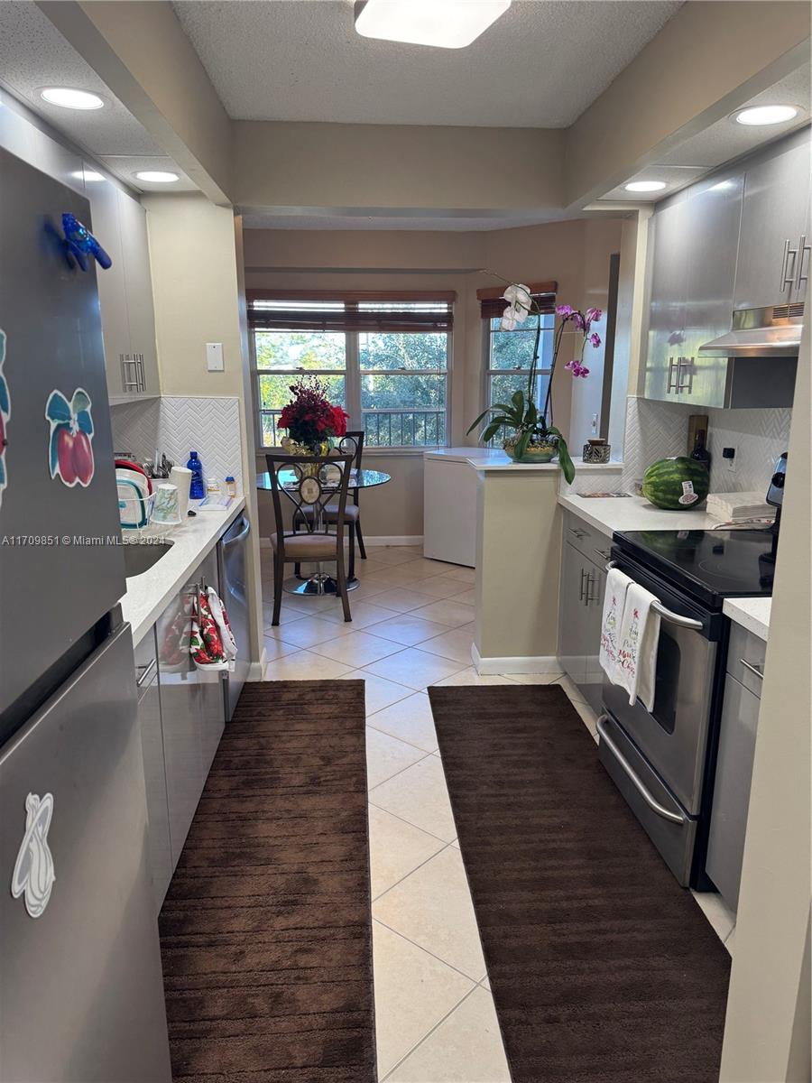 This galley kitchen features stainless steel appliances, light cabinetry, and an adjacent dining area — 12650 SW 6th St # 411K, Pembroke Pines FL 33027, PEMBROKE PINES, FL