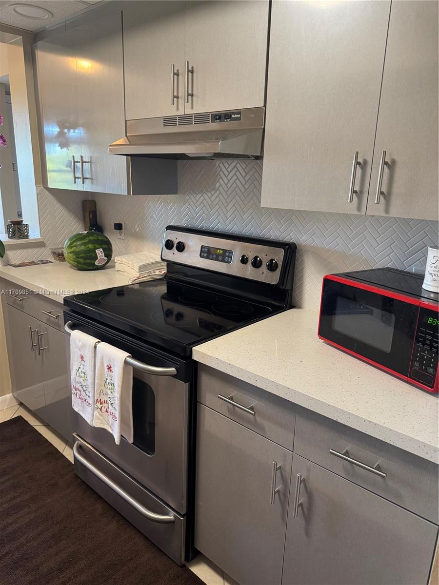 A kitchen features gray flat-panel cabinets, stainless steel appliances, and a white herringbone tile backsplash — 12650 SW 6th St # 411K, Pembroke Pines FL 33027, PEMBROKE PINES, FL