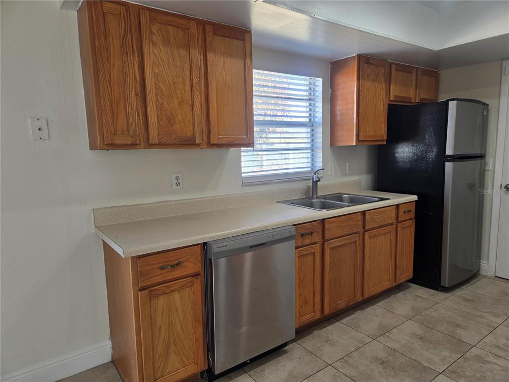 A kitchen features wood cabinets, a stainless steel dishwasher, a black refrigerator, and tile flooring — 271 LA PAZ DRIVE, KISSIMMEE, FL