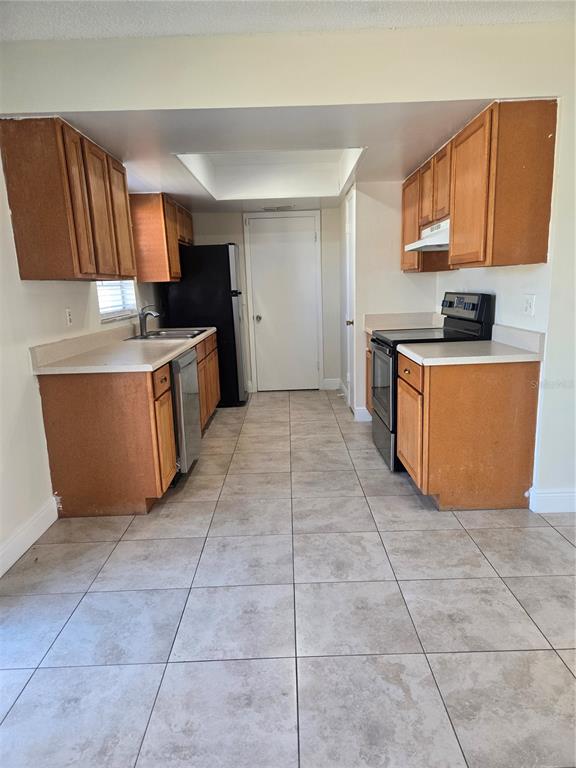 A galley kitchen features wood cabinets, light countertops, black appliances, and tiled flooring — 271 LA PAZ DRIVE, KISSIMMEE, FL