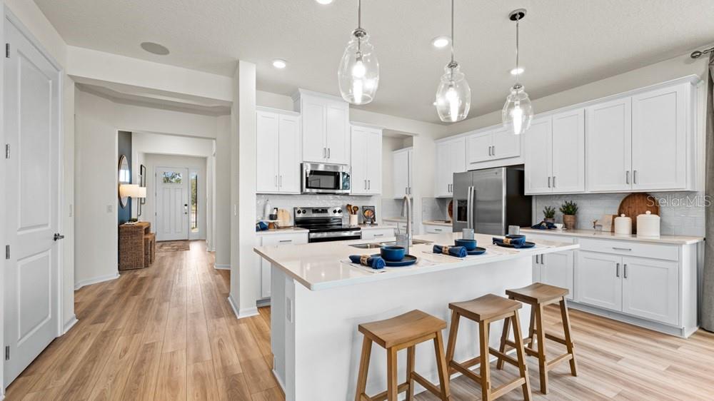 A modern kitchen features white cabinetry, a central island with bar stools, and wood flooring — 3512 LUMBER FALLS DRIVE, PLANT CITY, FL