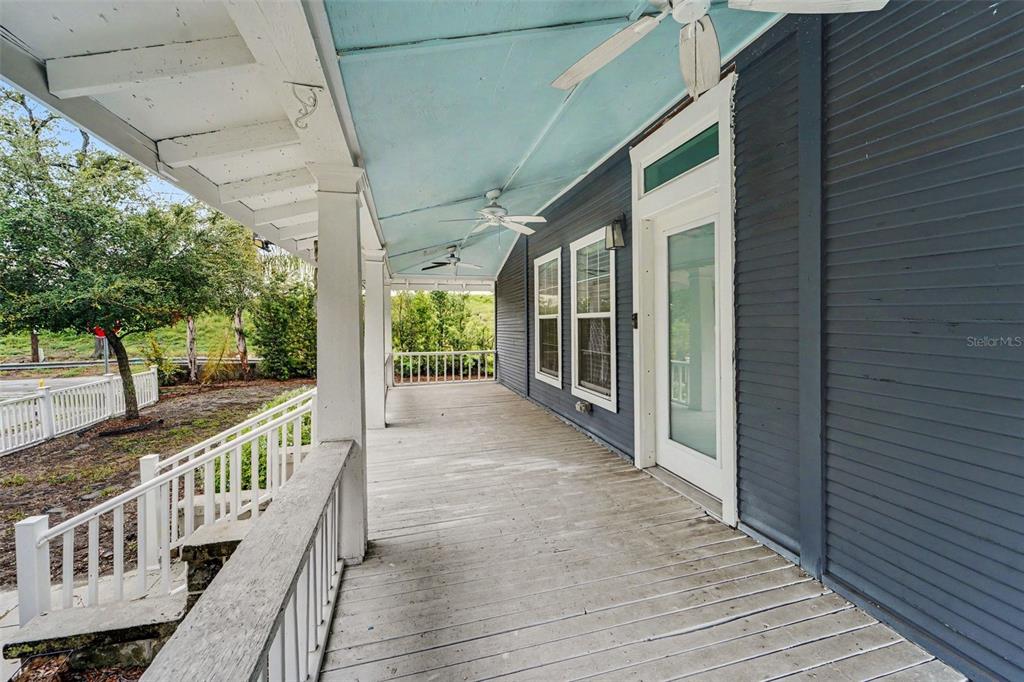 A long, covered wooden porch features white railings, ceiling fans, and dark gray horizontal siding — 800 E GENESEE STREET, TAMPA, FL