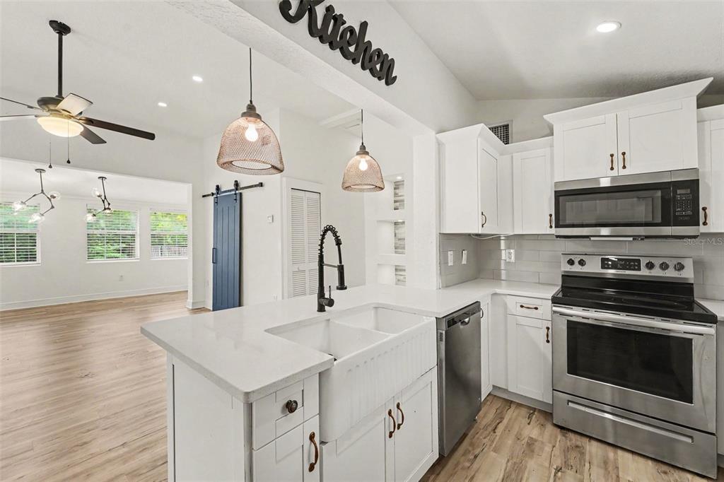 A modern kitchen features white cabinets, stainless steel appliances, a farmhouse sink, and wood flooring — 800 E GENESEE STREET, TAMPA, FL