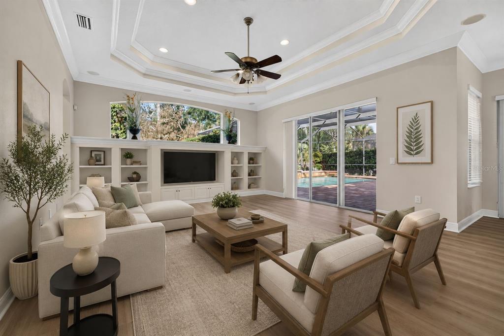 A living room with a tray ceiling, built-in shelving, a sectional sofa, and pool views — 5112 ABISHER WOOD LANE, BRANDON, FL