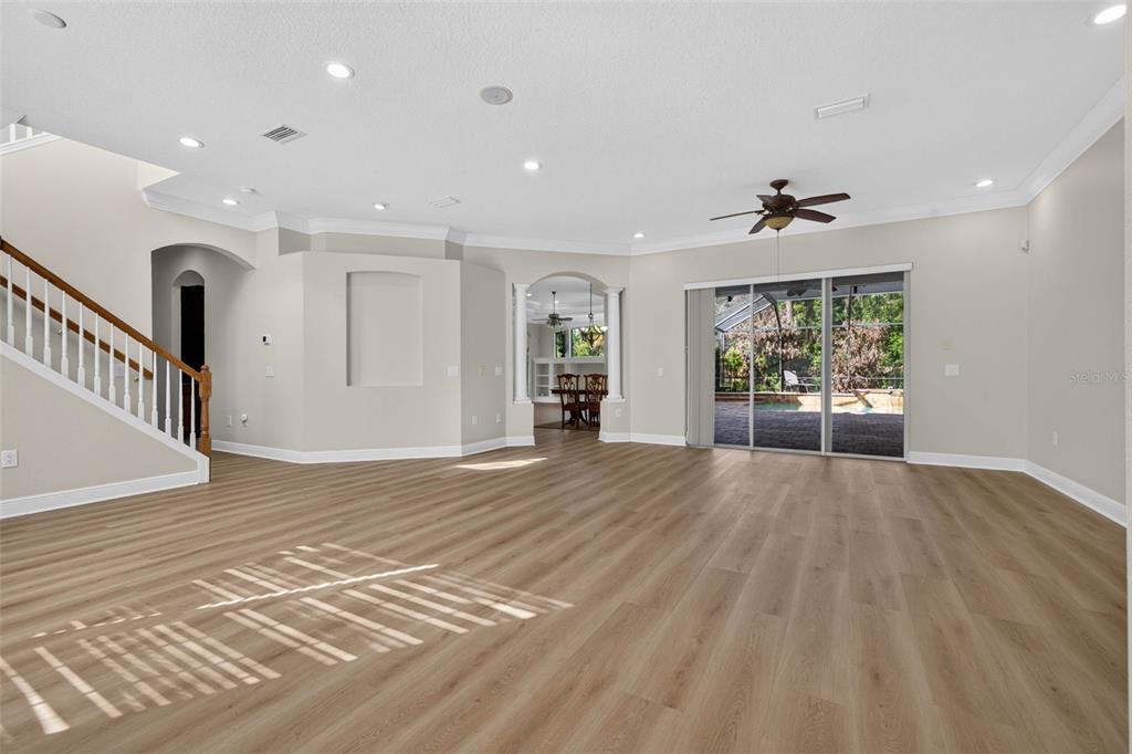 A spacious living room features light wood-look flooring, recessed lighting, a staircase, and sliding glass doors — 5112 ABISHER WOOD LANE, BRANDON, FL