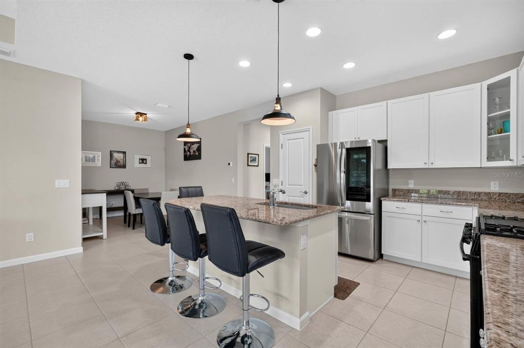 A kitchen with a granite island, black bar stools, white cabinets, and stainless steel appliances — 497 LOST SHAKER WAY, DAYTONA BEACH, FL