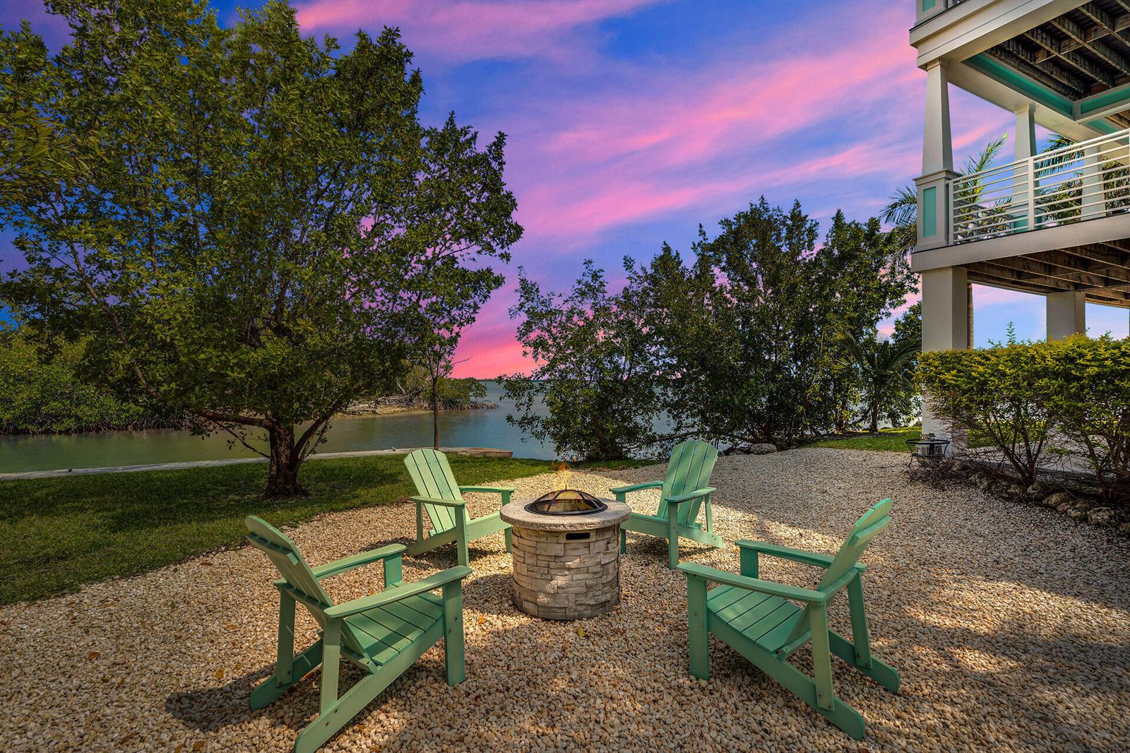 Four light green Adirondack chairs surround a stone fire pit on a gravel patio — 17387 Dolphin Street E, FL 33042, FL