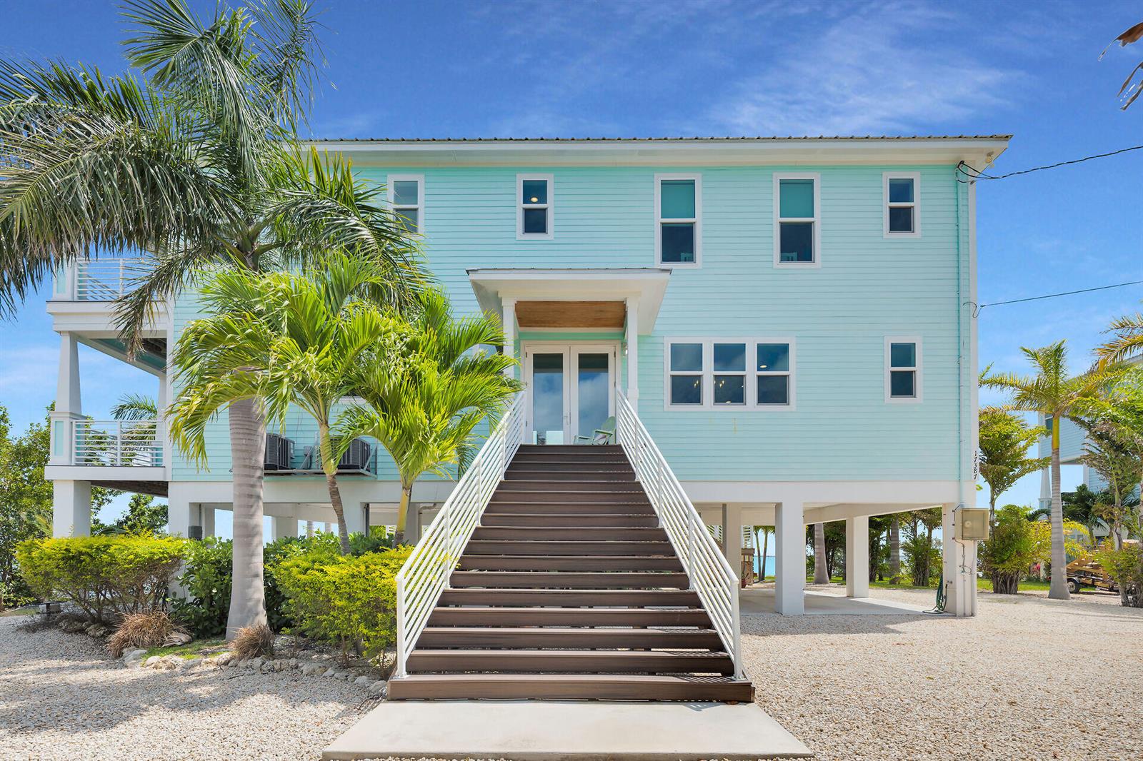 A light blue elevated house features a central staircase leading to double front entry doors — 17387 Dolphin Street E, FL 33042, FL