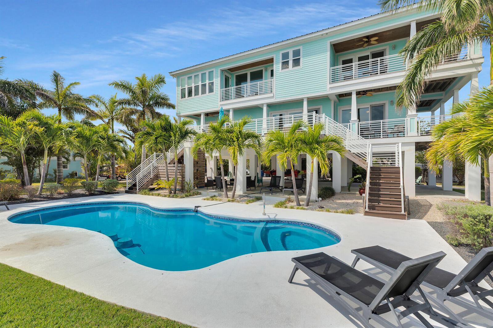 A light blue elevated house features a swimming pool and lounge chairs in the backyard — 17387 Dolphin Street E, FL 33042, FL