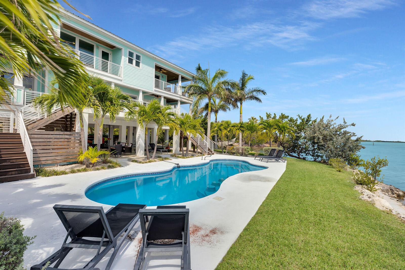 A light blue multi-story house overlooks a swimming pool and a grassy waterfront yard — 17387 Dolphin Street E, FL 33042, FL