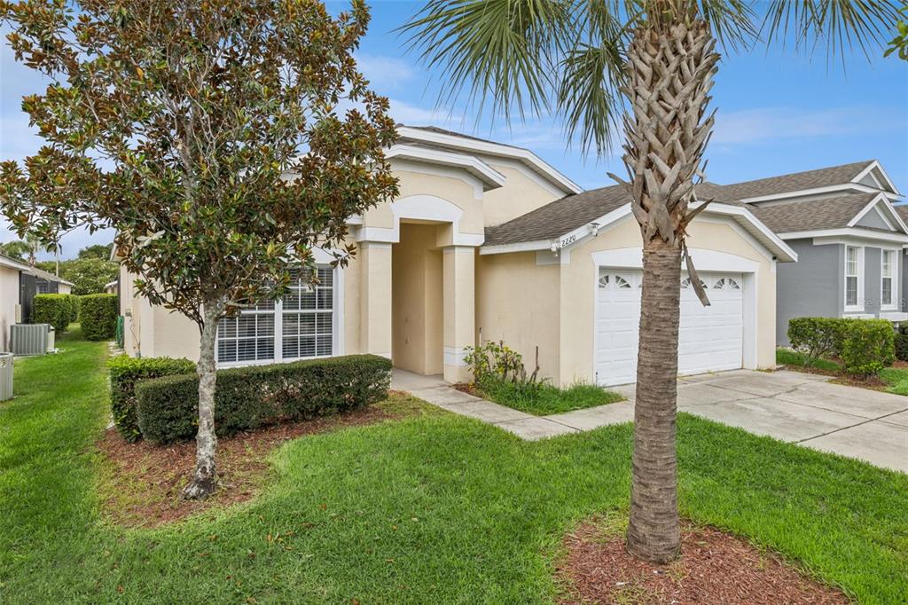 A single-story house with a beige stucco exterior, a two-car garage, and a palm tree — 2220 WYNDHAM PALMS WAY, KISSIMMEE, FL