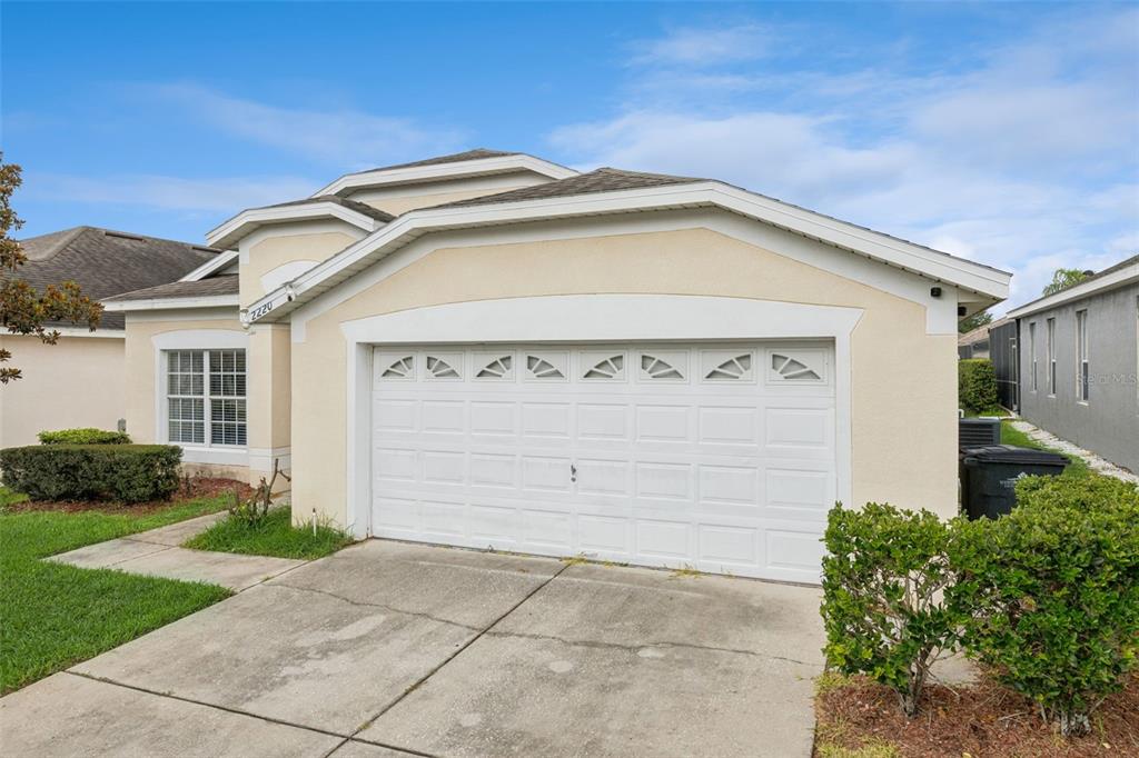 A beige single-story house features a two-car garage and a concrete driveway — 2220 WYNDHAM PALMS WAY, KISSIMMEE, FL