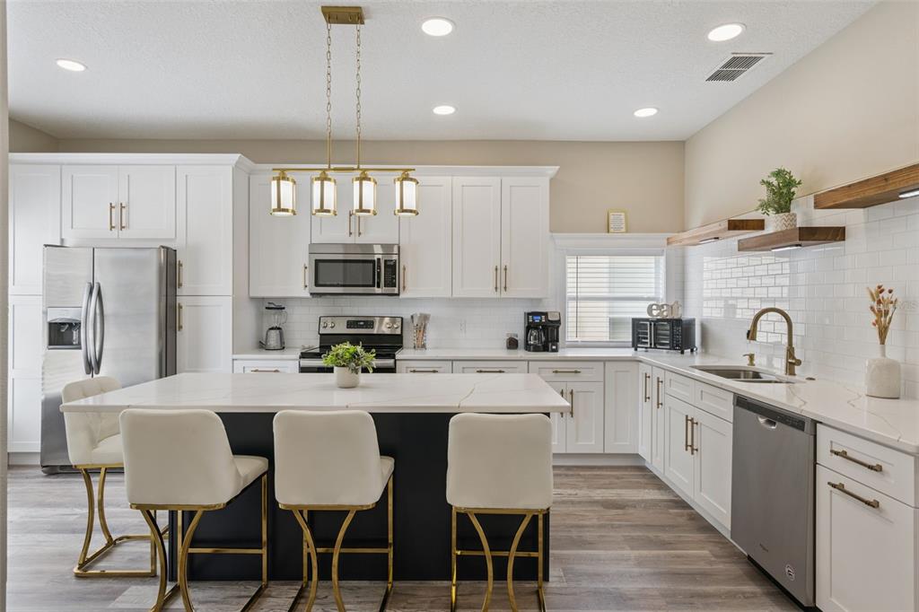 A modern kitchen features white cabinetry, a dark island with bar stools, and gold accents — 2220 WYNDHAM PALMS WAY, KISSIMMEE, FL