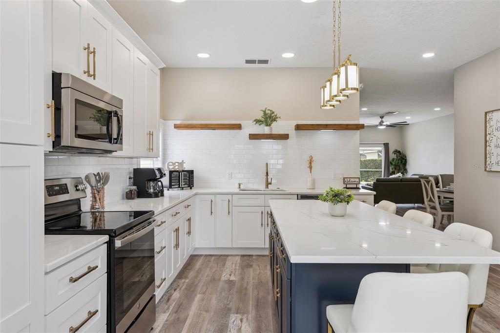 A modern kitchen features white cabinets, a navy island, quartz countertops, and wood floating shelves — 2220 WYNDHAM PALMS WAY, KISSIMMEE, FL