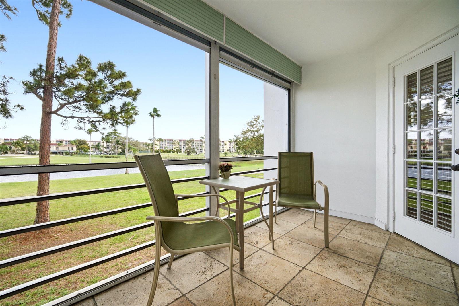 A screened-in balcony features tile flooring, two chairs, a small table, and golf course views — 3593 Birdie Drive # 203, Lake Worth FL 33467, LAKE WORTH, FL