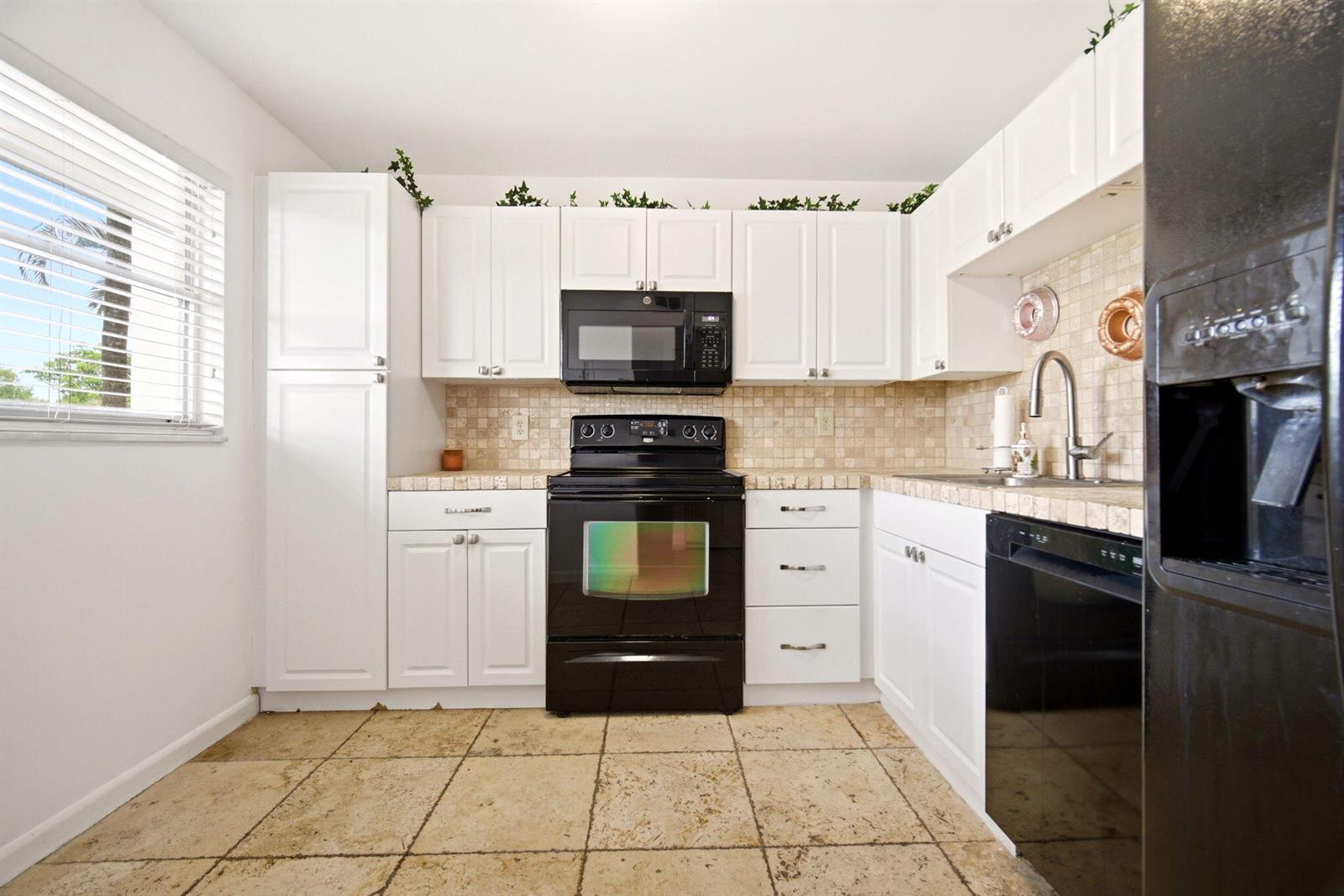 A kitchen features white cabinets, black appliances, a tiled backsplash, and light-colored stone floor tiles — 3593 Birdie Drive # 203, Lake Worth FL 33467, LAKE WORTH, FL