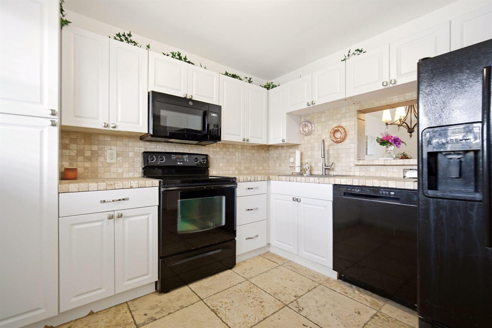 A kitchen features white cabinets, black appliances, tile countertops, and a tile floor — 3593 Birdie Drive # 203, Lake Worth FL 33467, LAKE WORTH, FL
