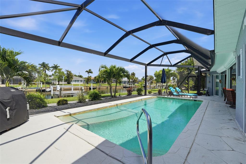 A screened-in swimming pool patio overlooks a canal with boat docks and palm trees — 300 DELIDO COURT, PUNTA GORDA, FL