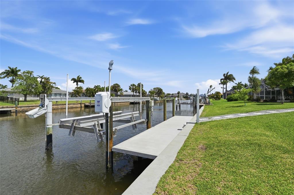 A boat lift sits in a canal next to a concrete dock and grassy lawn — 300 DELIDO COURT, PUNTA GORDA, FL