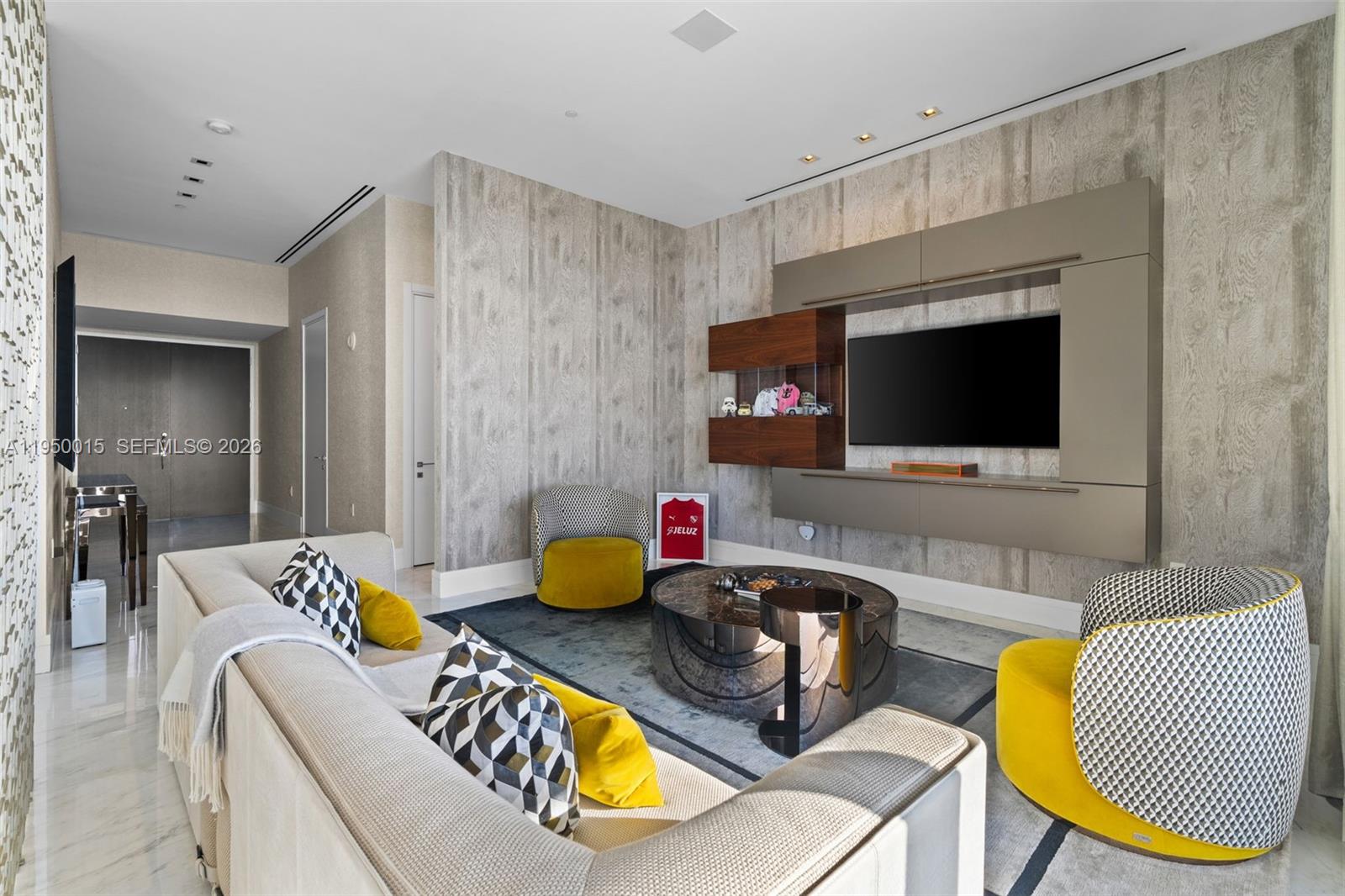 A modern living room features a large sectional, yellow accent chairs, and a wall-mounted television — 17141 Collins Ave # 3002, Sunny Isles Beach FL 33160, SUNNY ISLES BEACH, FL