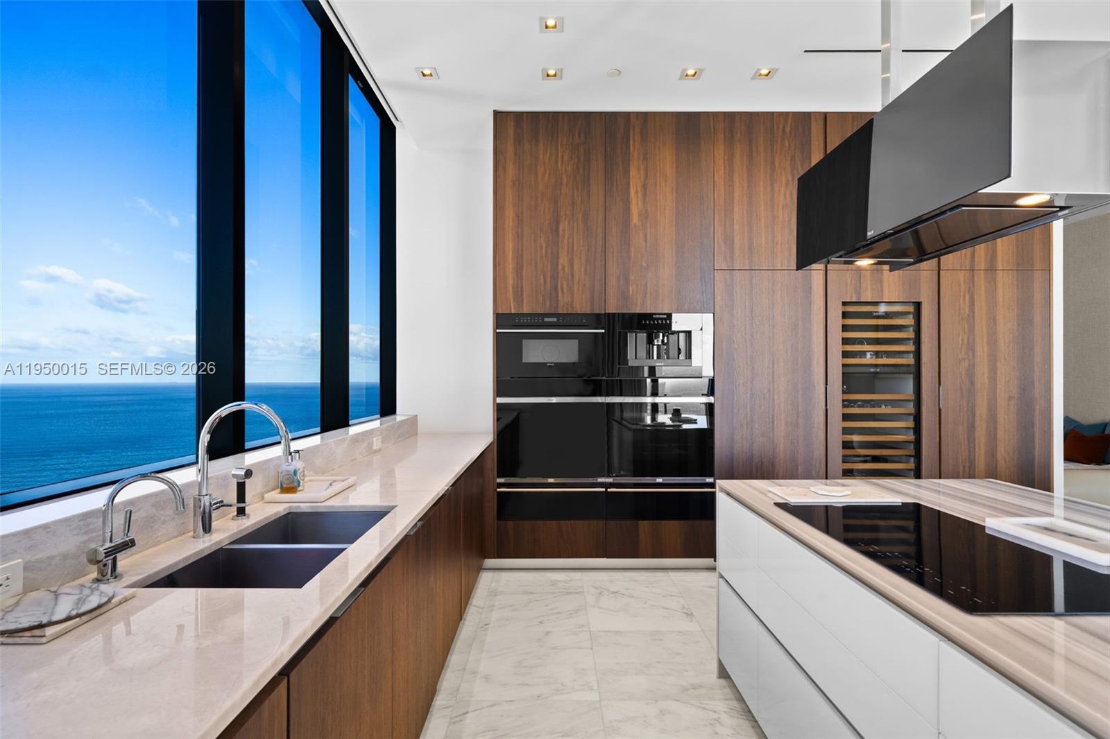 A modern kitchen features wood cabinetry, marble countertops, a center island, and floor-to-ceiling ocean views — 17141 Collins Ave # 3002, Sunny Isles Beach FL 33160, SUNNY ISLES BEACH, FL