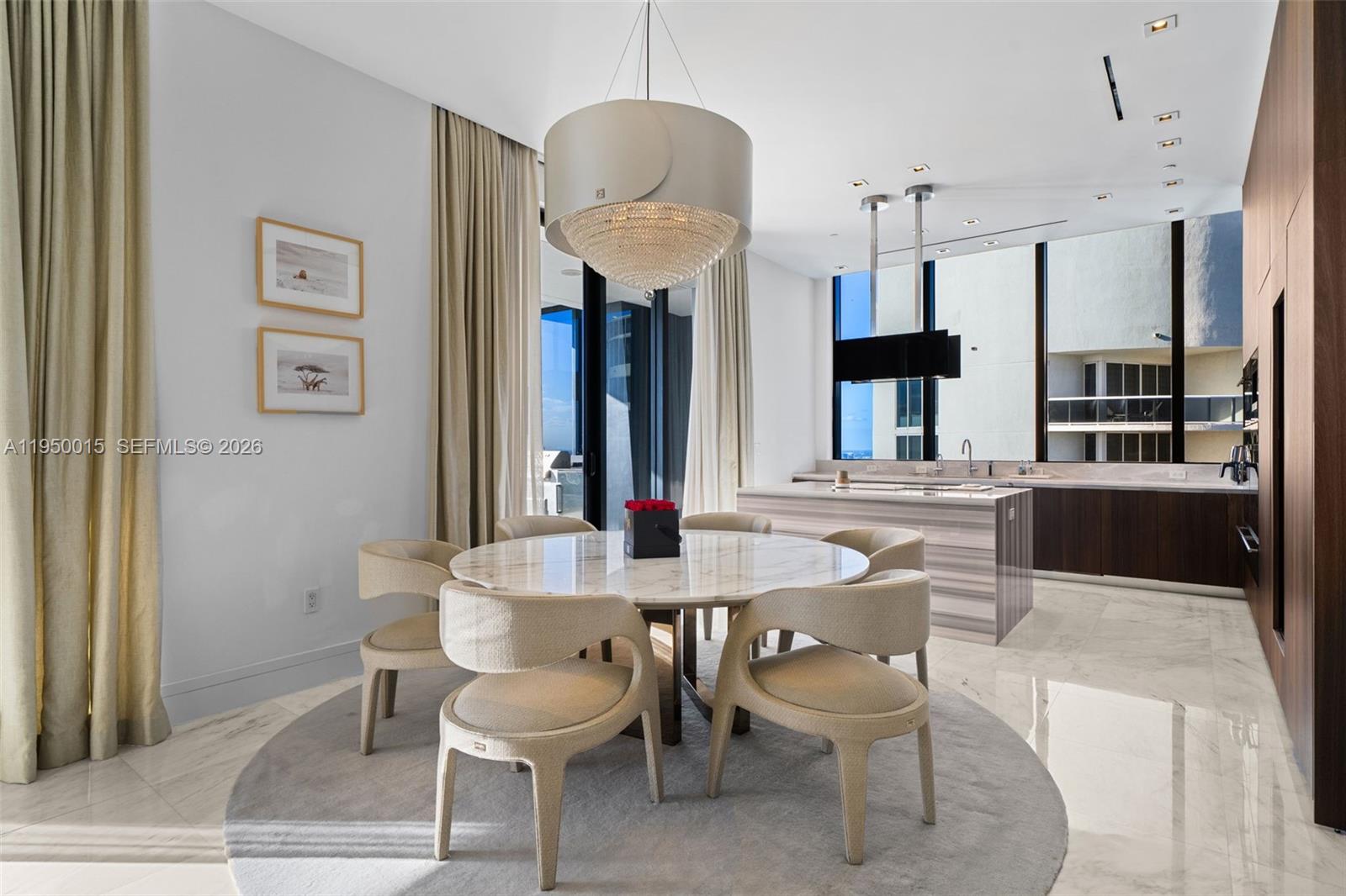 A dining area with a marble table, modern chairs, and a chandelier near a kitchen — 17141 Collins Ave # 3002, Sunny Isles Beach FL 33160, SUNNY ISLES BEACH, FL