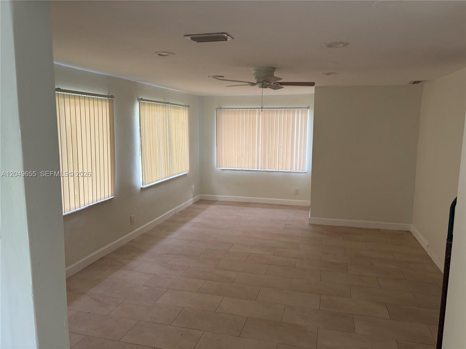 An empty room features light-colored tile flooring, vertical blinds on three windows, and a ceiling fan — 5853 Mckinley St # 3, Hollywood FL 33021, HOLLYWOOD, FL