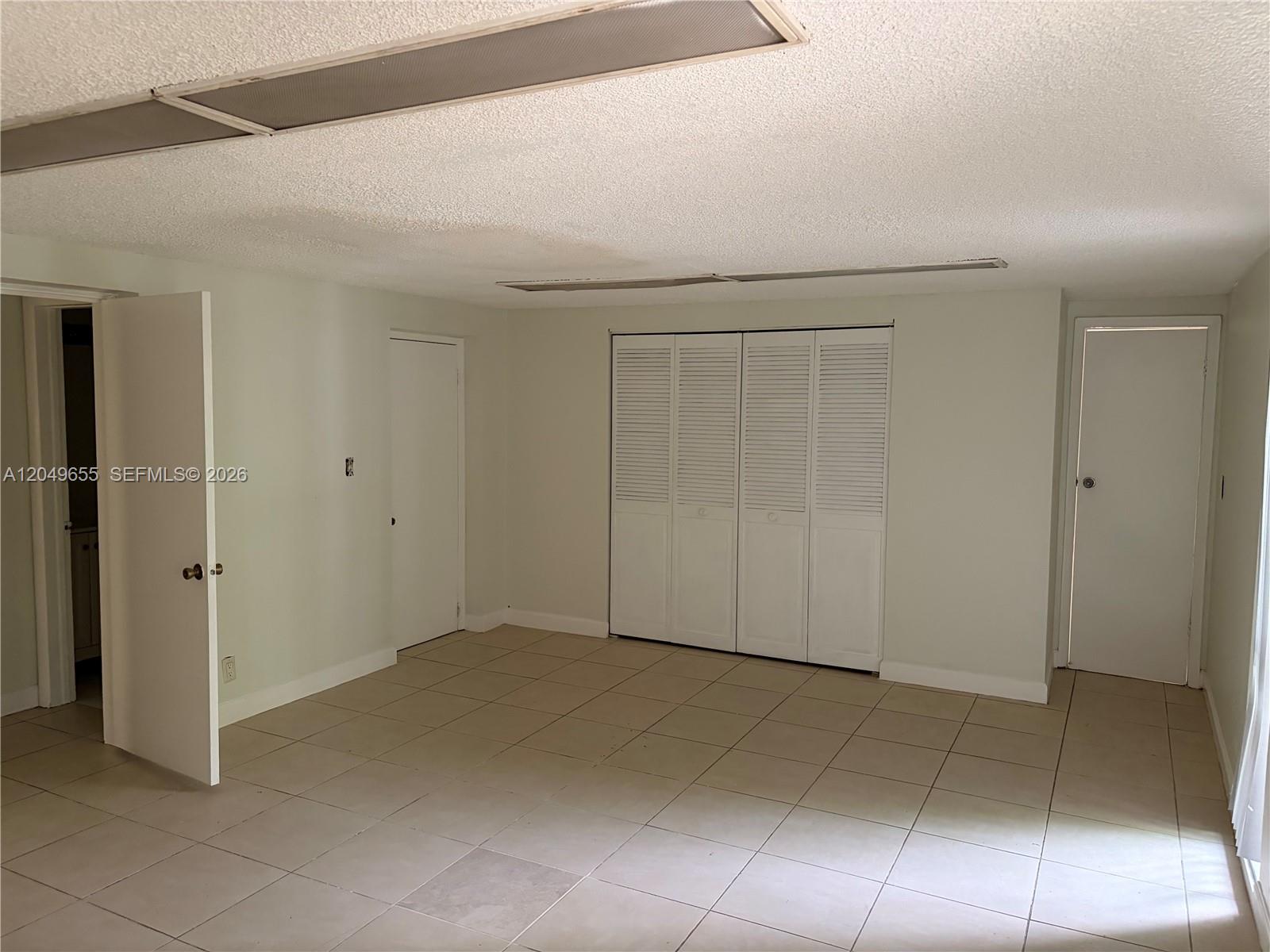 This room features light-colored tile flooring, white walls, a popcorn ceiling, and multiple closet doors — 5853 Mckinley St # 3, Hollywood FL 33021, HOLLYWOOD, FL