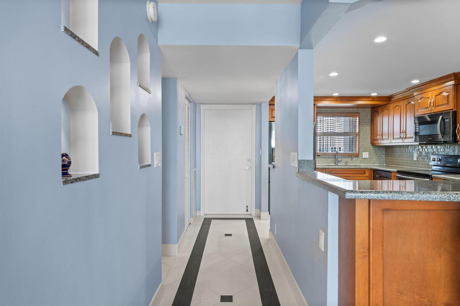 A hallway with arched wall niches leads to a white door next to a kitchen — 511 Bayshore Drive # 904, Fort Lauderdale FL 33304, FORT LAUDERDALE, FL