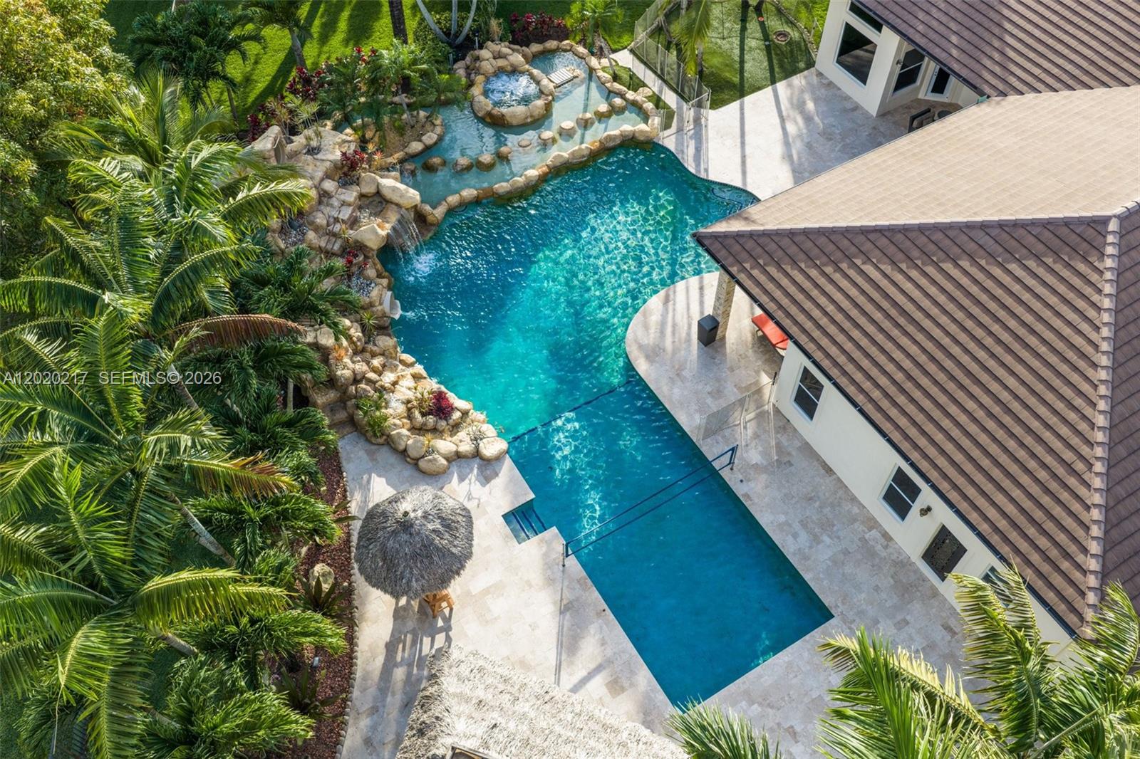 An aerial view shows a swimming pool with a rock waterfall, spa, and patio area — 10018 Laurel Rd, Davie FL 33328, DAVIE, FL
