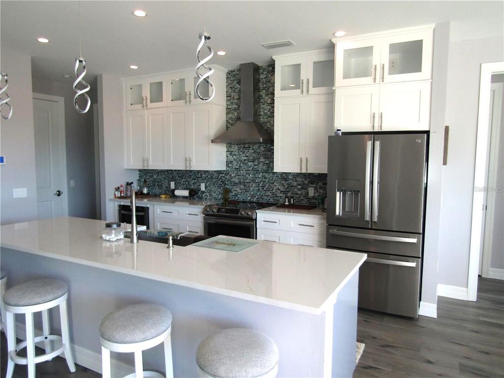 A modern kitchen features white cabinets, a quartz island, stainless steel appliances, and a tiled backsplash — 2064 LITTLE PINE CIRCLE, PUNTA GORDA, FL