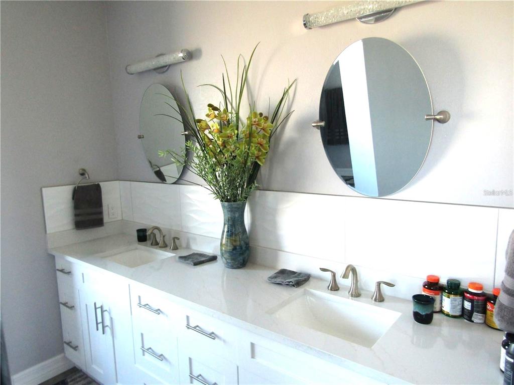 A double-vanity bathroom features white cabinets, a quartz countertop, and two round wall mirrors — 2064 LITTLE PINE CIRCLE, PUNTA GORDA, FL