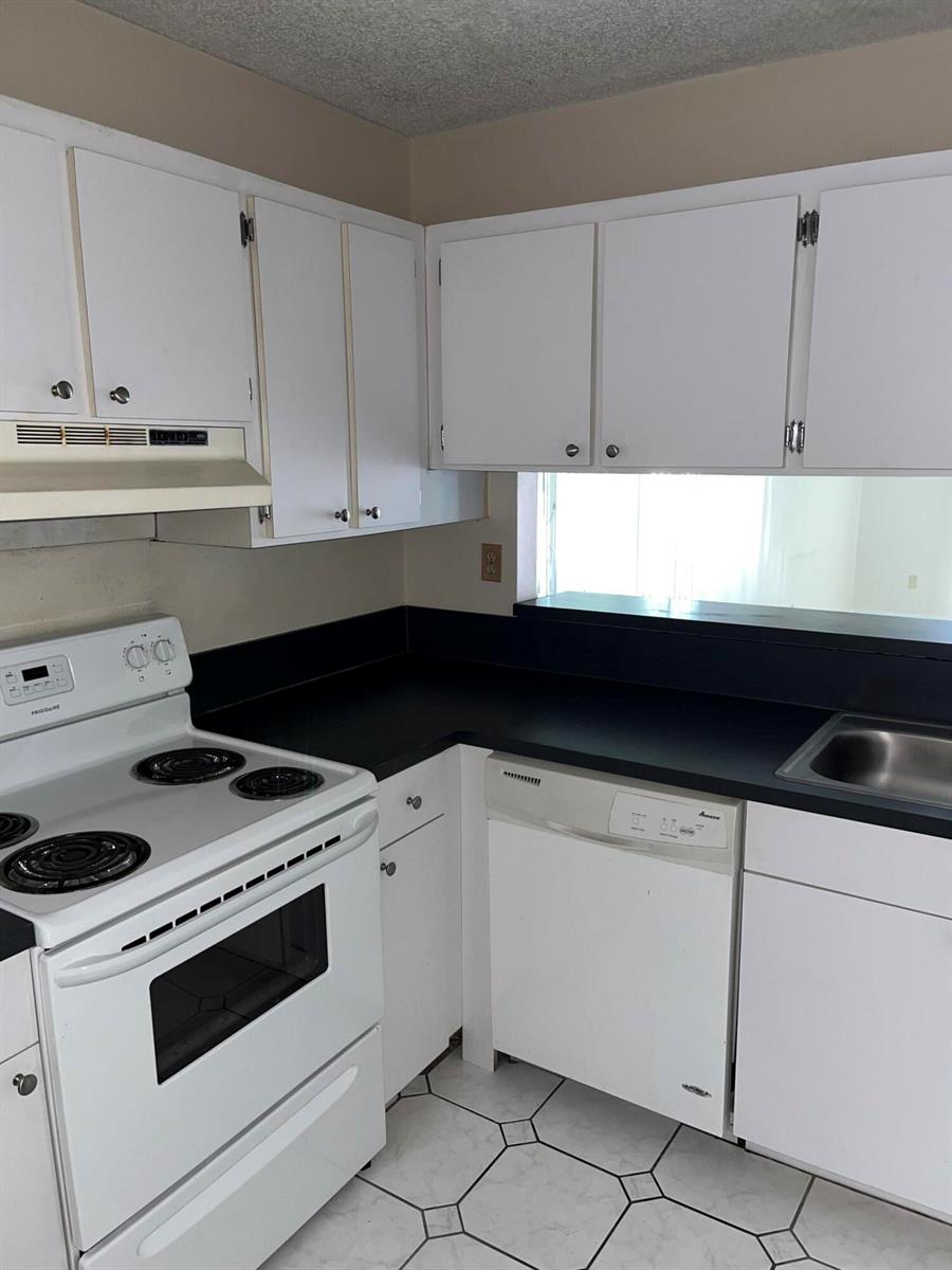 A kitchen features white cabinets, black countertops, a white stove, and a white dishwasher — 3396 Foxcroft Road # 309, Miramar FL 33025, MIRAMAR, FL