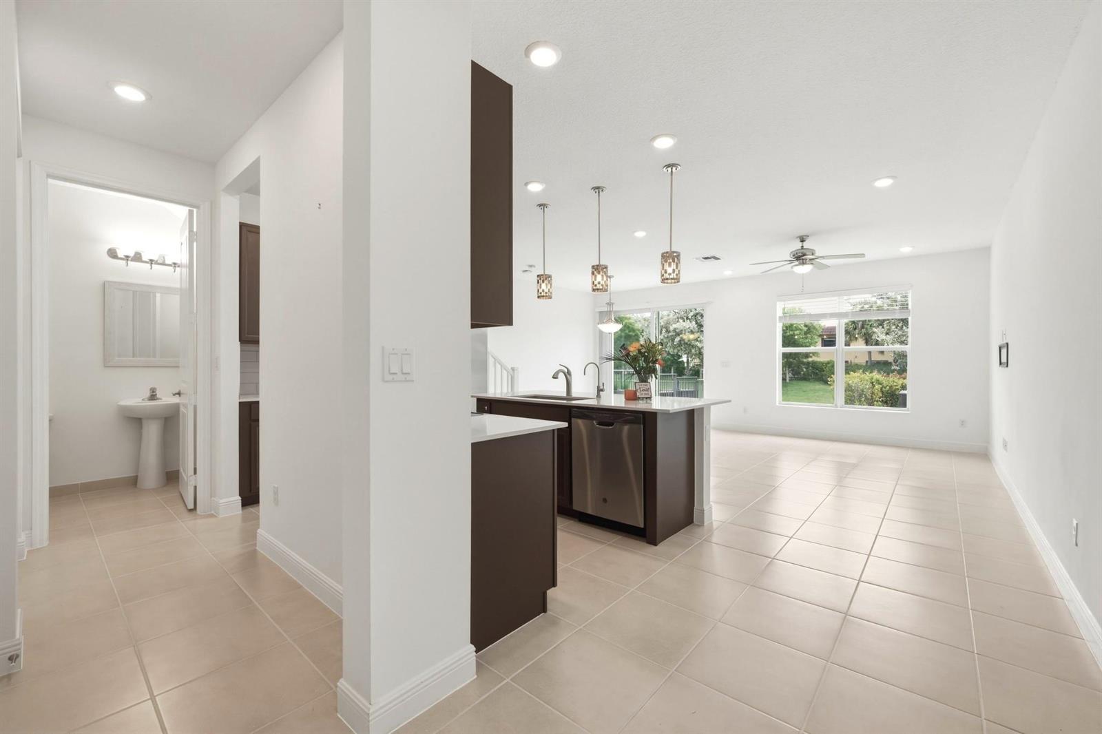 A kitchen with dark cabinets and a stainless steel dishwasher opens to a living area — 4364 Veleiros Avenue, Deerfield Beach FL 33064, DEERFIELD BEACH, FL